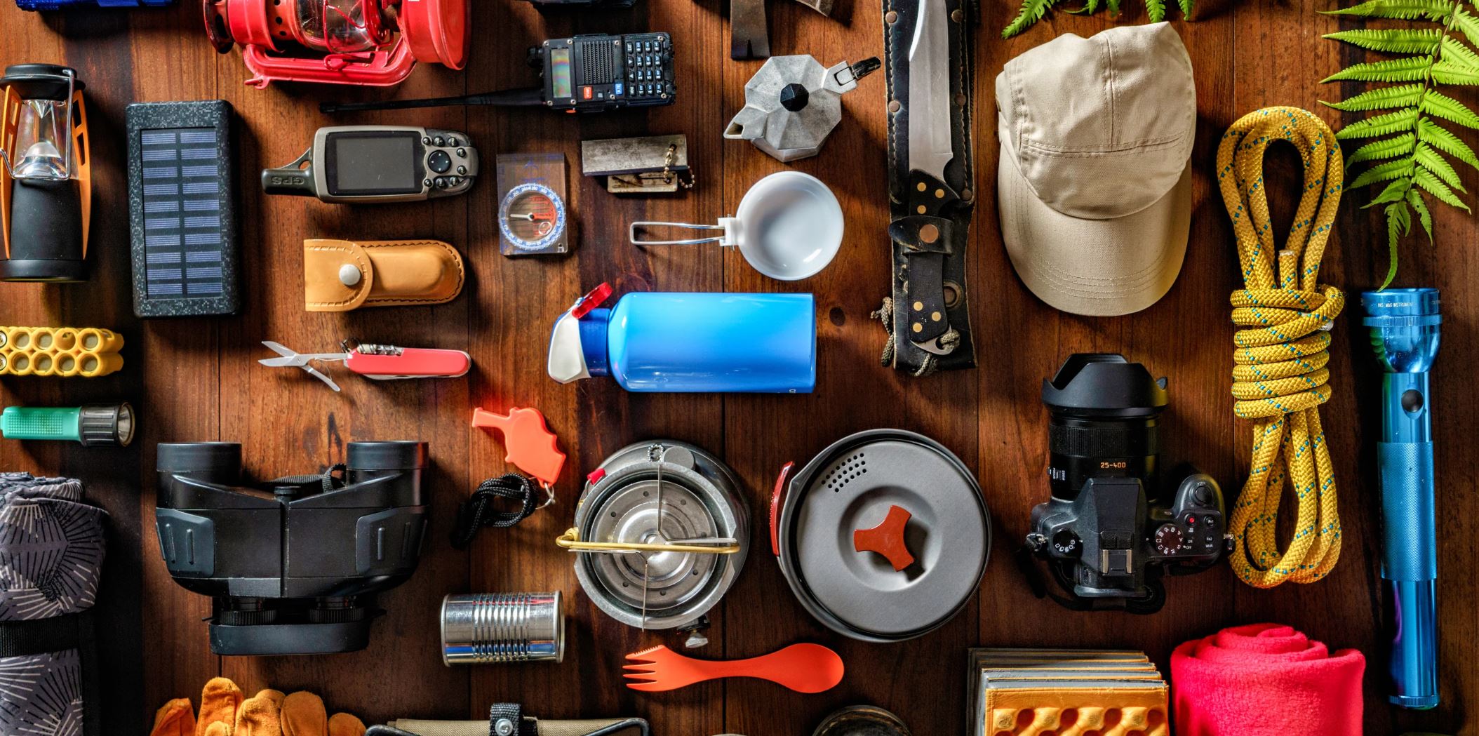 Overland and camping gear laid out on a wood floor — lanterns, GPS, stove, cookset, rope, camera, binoculars
